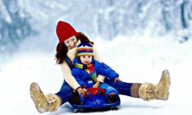 Mom and child riding down a hill on a sled.